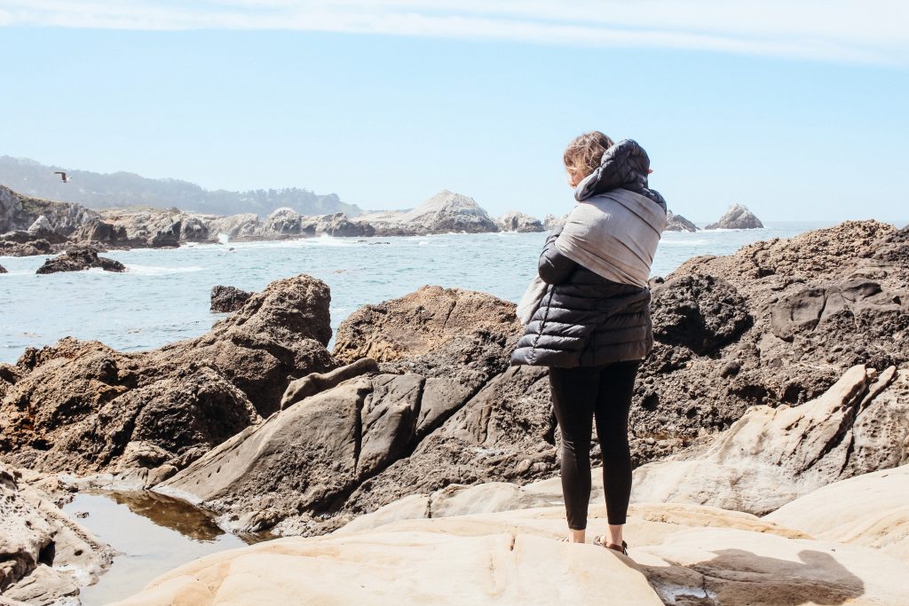 woman with baby in sling overlooking ocean