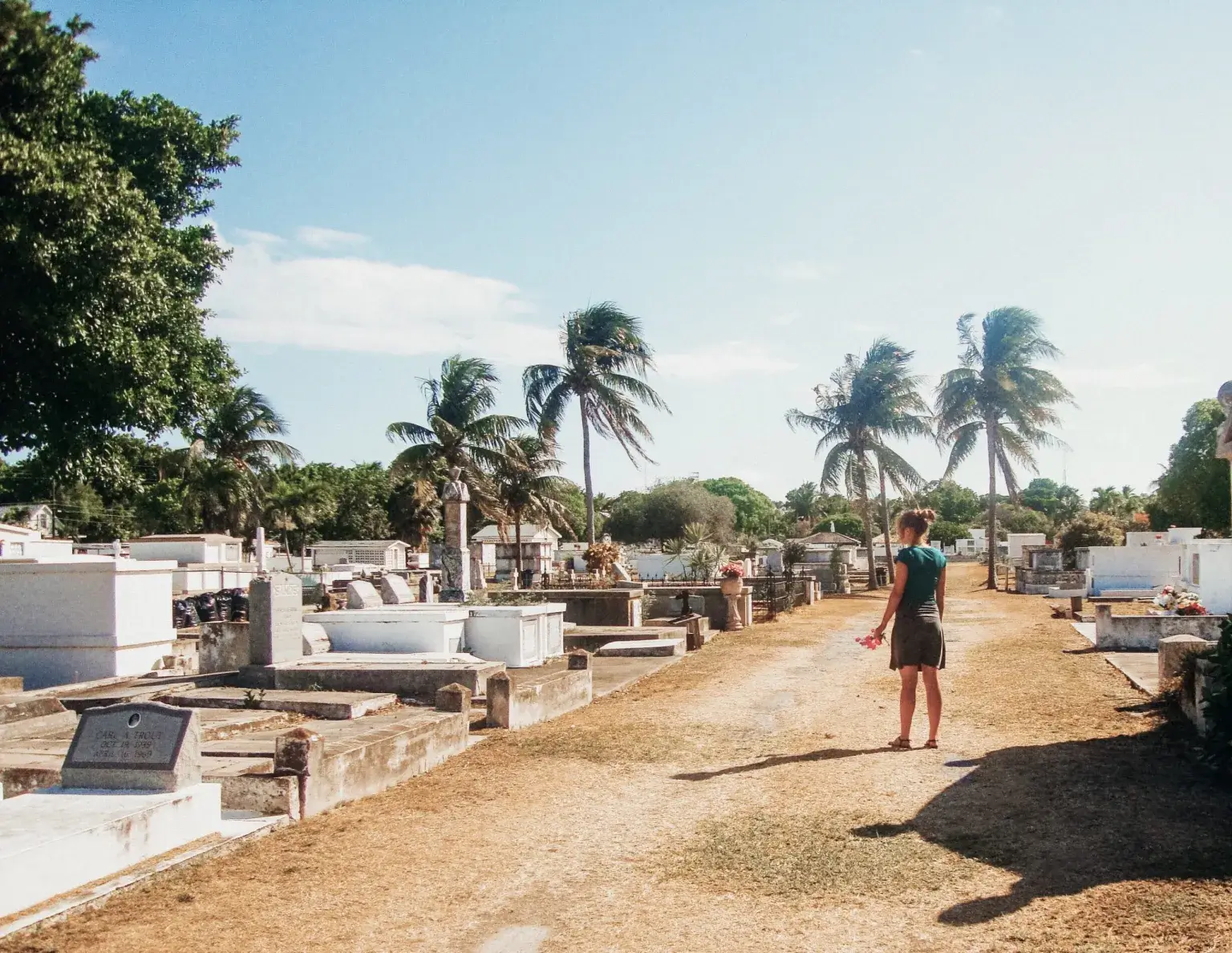Woman standing in an old cemetery in Key West Florida with white-washed grave markings and palm trees