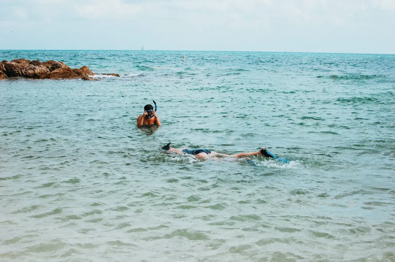 Two people snorkeling at Fort Zachary Taylor State Park in crystal blue ocean water.