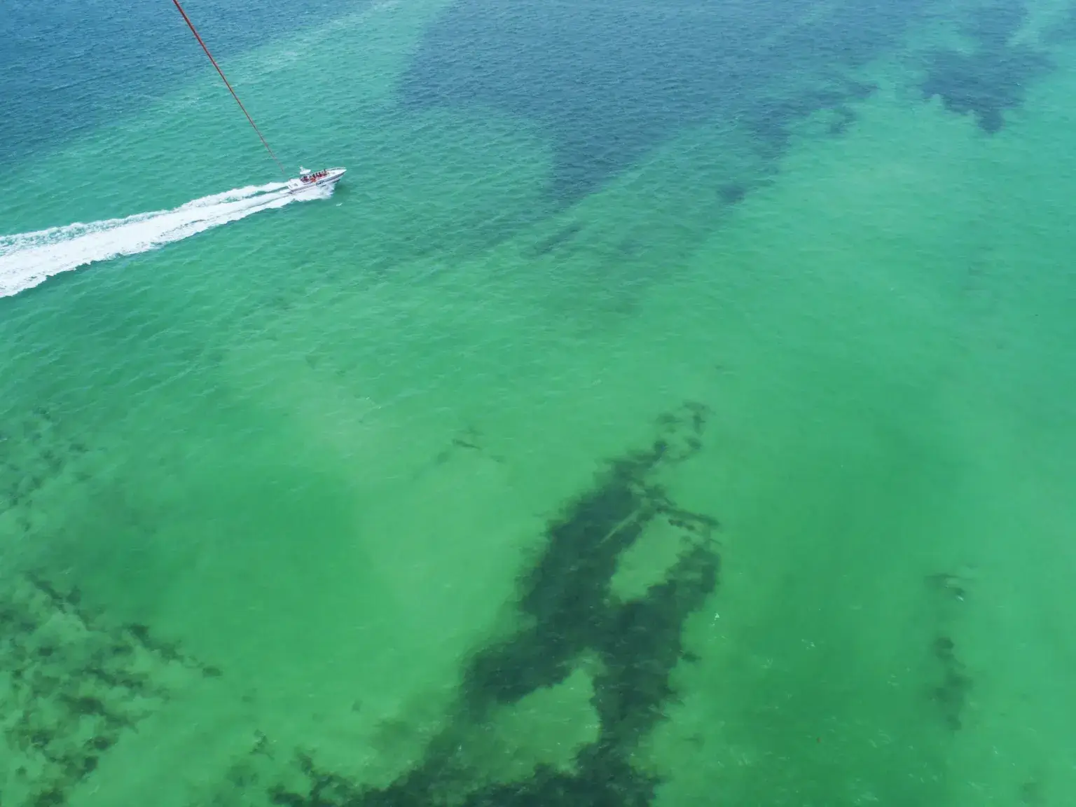 Picture looking down at a small boat from a parasail over emerald-green waters