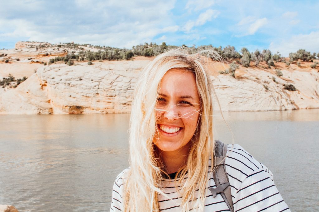 Woman facing camera in front of reservoir surrounded by sandstone