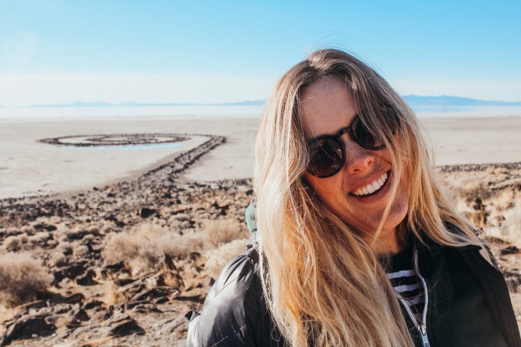 Woman with sunglasses in front of a large jetty made of rocks shaped in a spiral