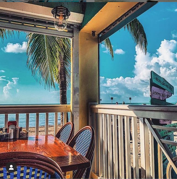 Key West food on the beach. Dining table on beach-side patio with palm tree and beach signs. 