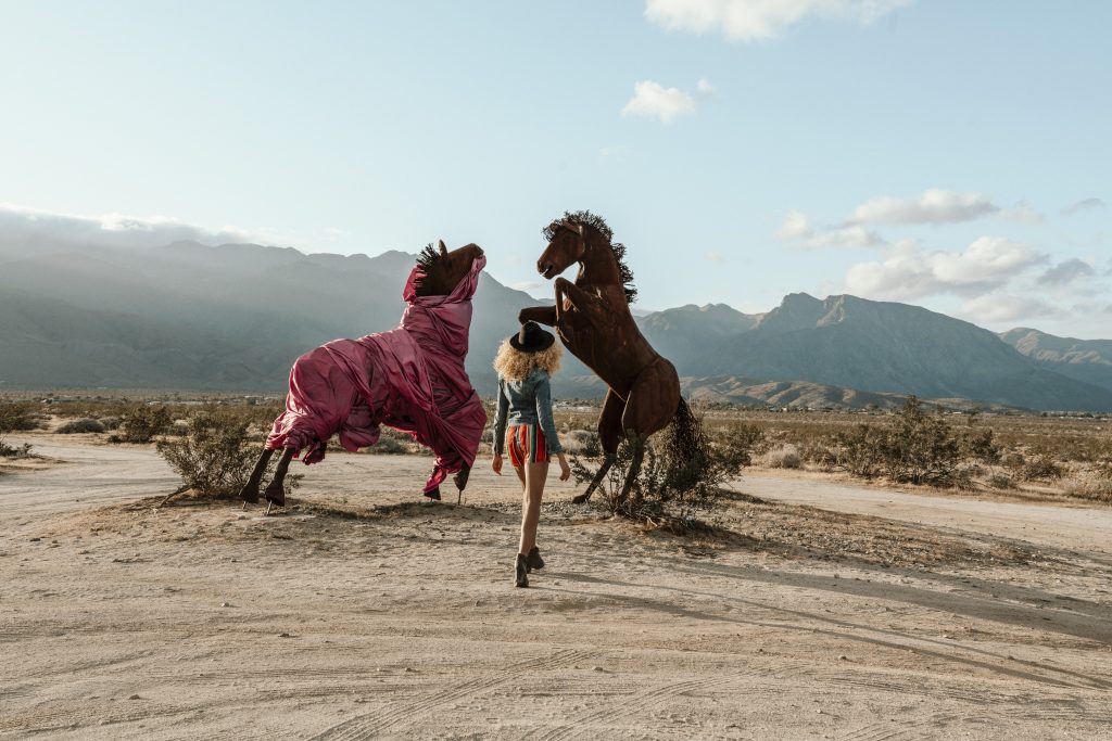 Woman standing in front of large iron horse sculptures in the desert at Anza-Borrego State Park in California