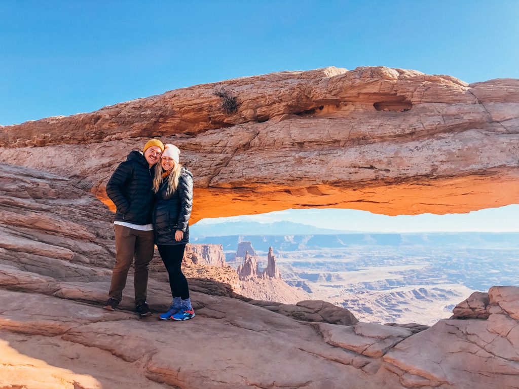 Man and woman in front of sandstone arch with view of desert floor