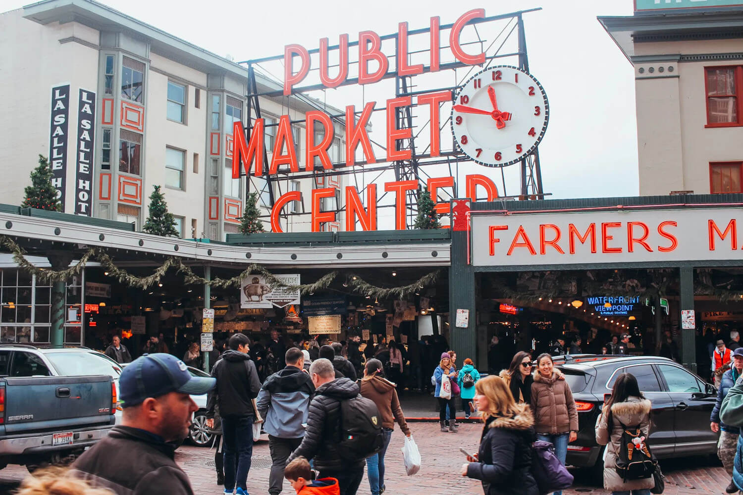 Large red, neon sign atop a building that reads Pubic Market Center. Pike Place Market is the best place to start your day trip to Seattle