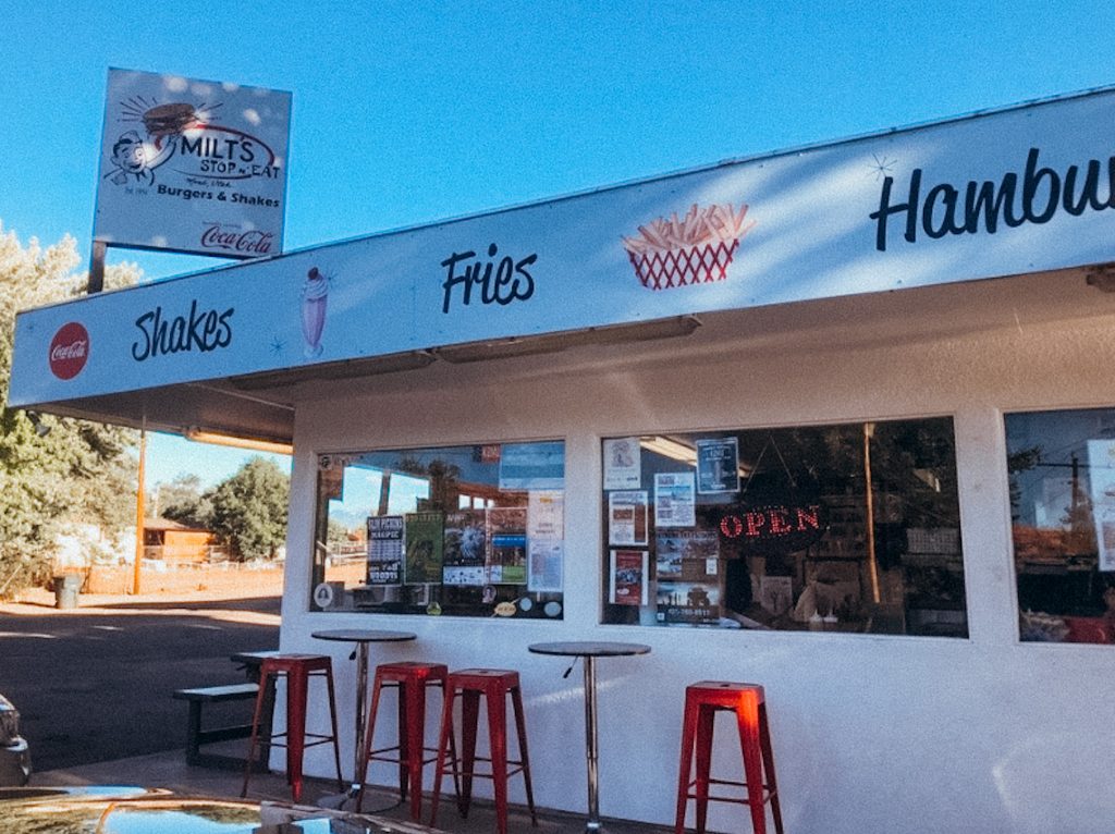 White building with tables and chairs out front with signs reading 'shakes' 'fries' and hamburgers