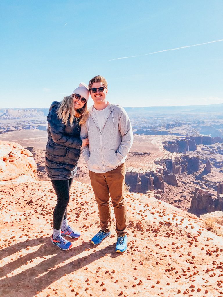 Man and woman stand in front of overlook of huge sandstone canyon