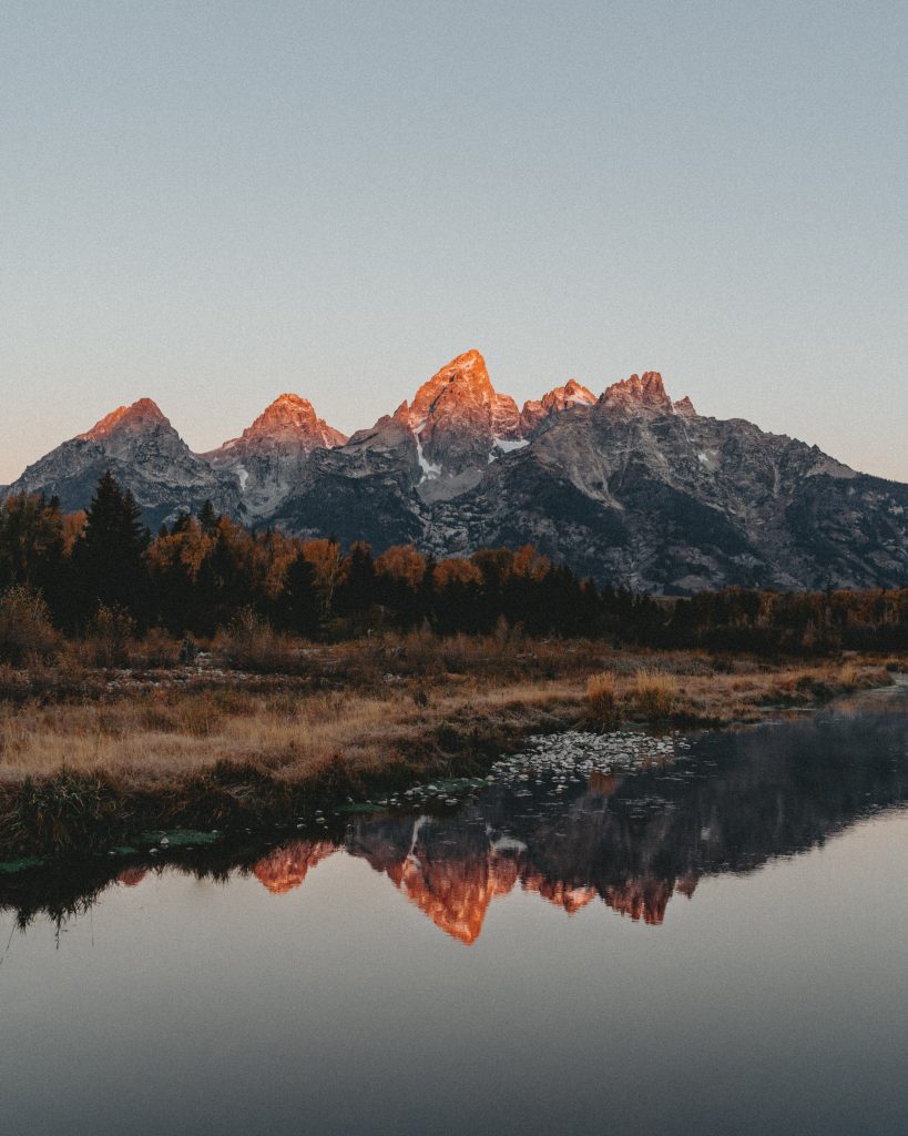 5 mountain peaks reflect into river at sunset
