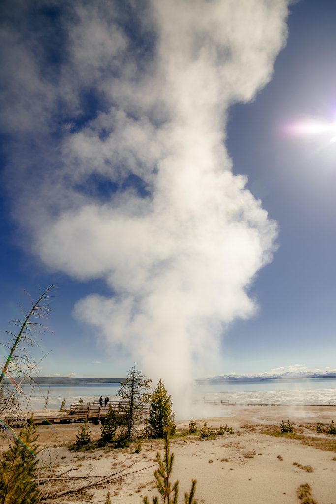 Steam comes out of ground in Yellowstone National Park with blue lake in the background