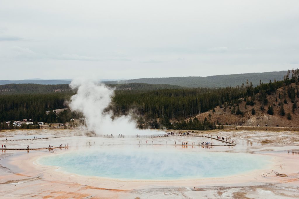 Large natural pool of water colored orange, yellow green and blue with steam rising in Yellowstone