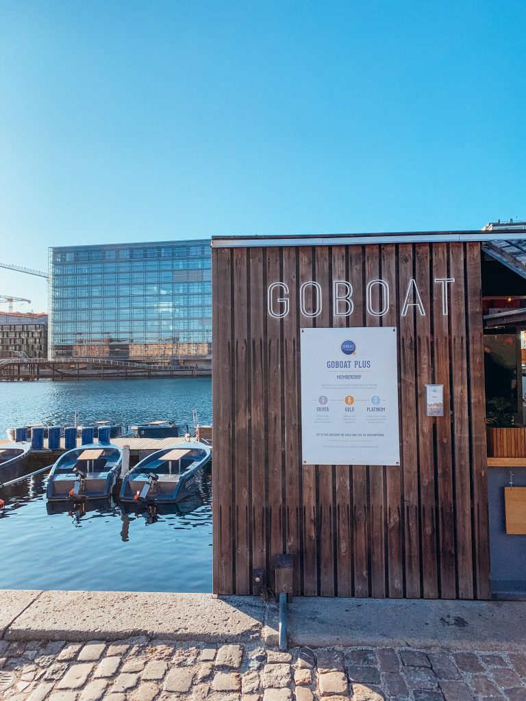 Small wooden building with a sign that reads 'GOBOAT' with small blue boats on the water next to it