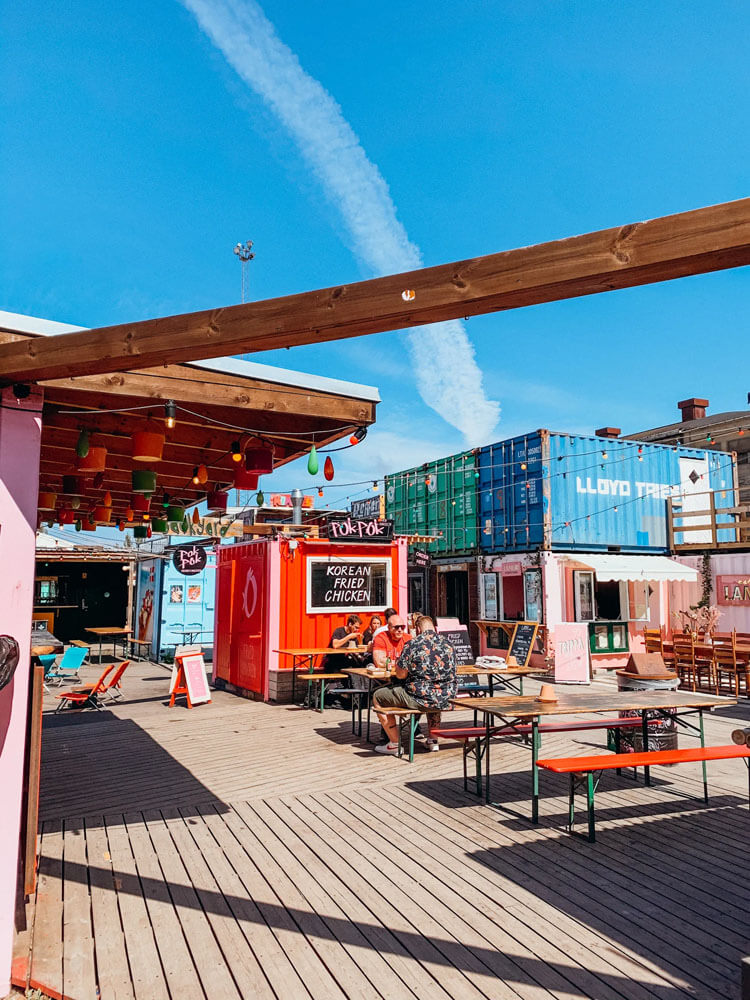 Colorful train car boxes converted into small food stalls with picnic tables and hanging lights