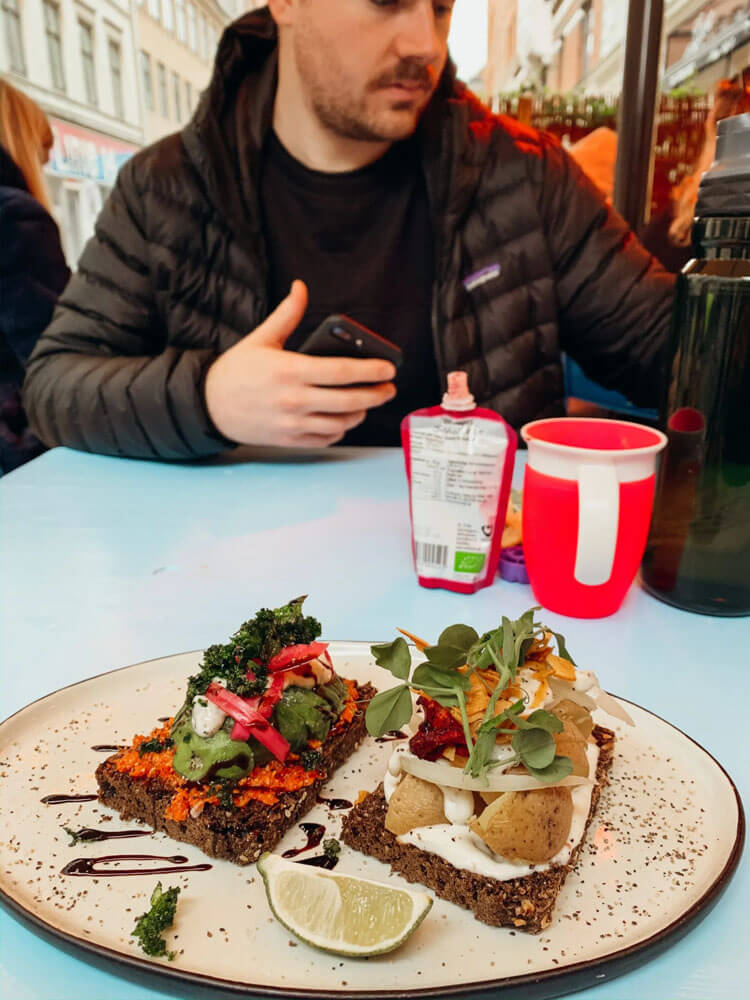 Veggies on top of brown rye bread on tan plate on blue table 
