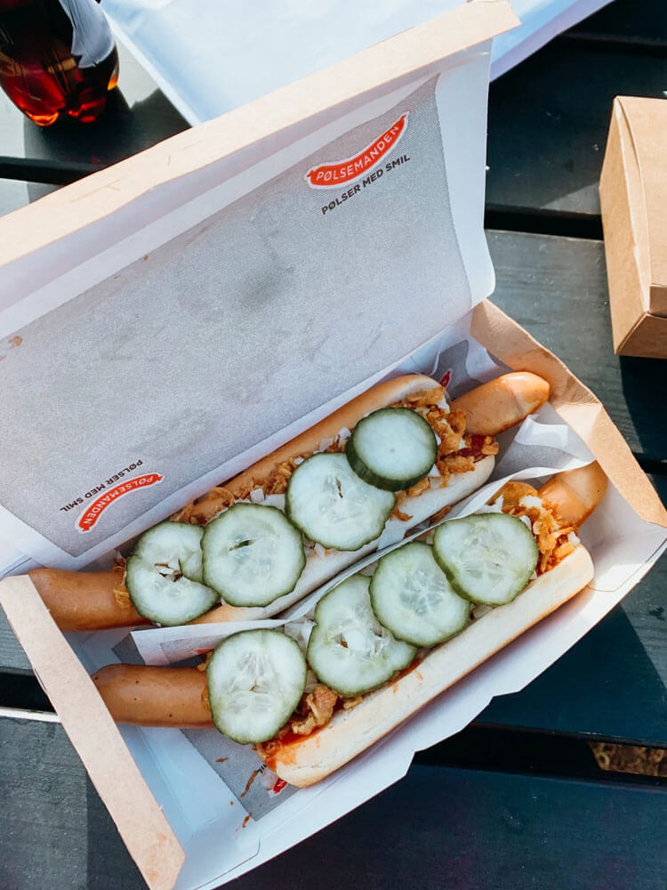 Two hot dogs in buns with pickles on top in cardboard box