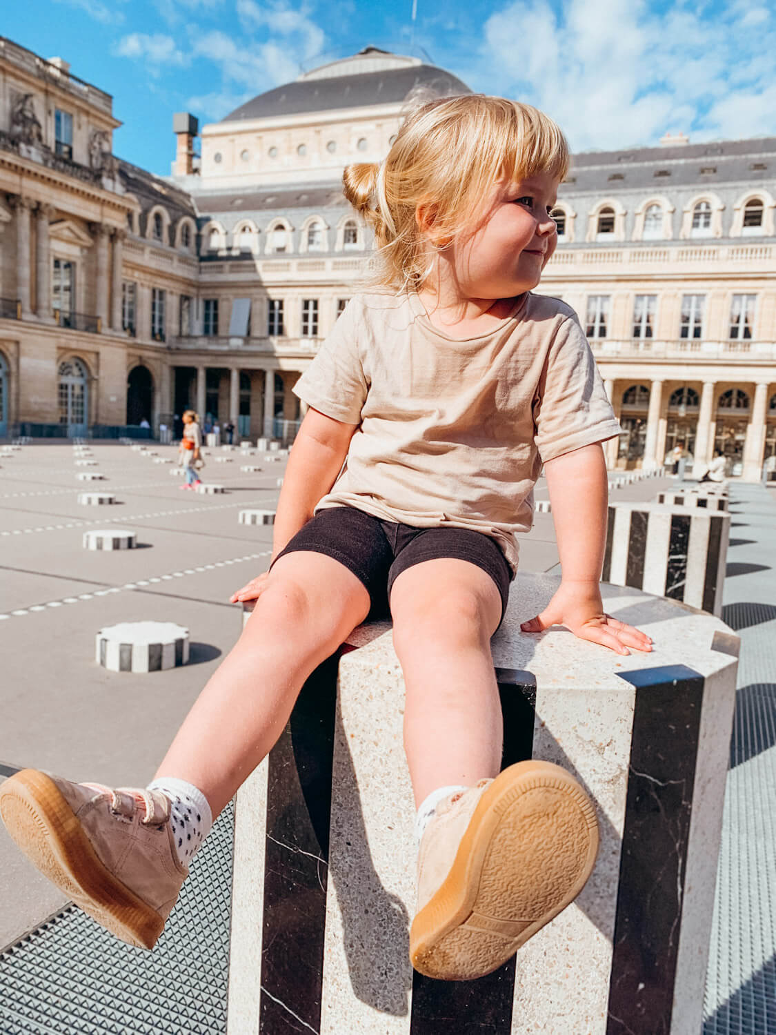 Young child sits on top of white and black striped column in Paris