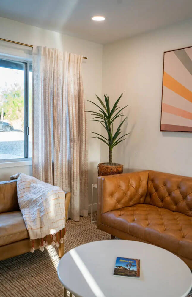Two brown couches with a painting of a sunset on the wall