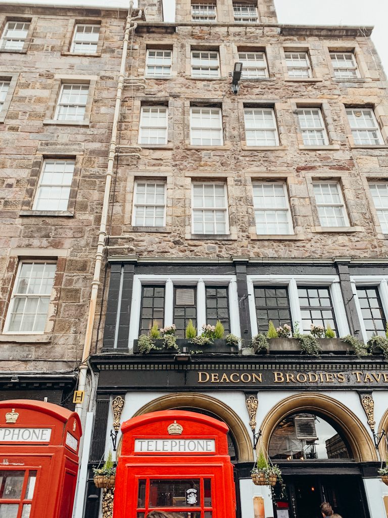 Red and white phone booth in front of grey brick building with a white and back storefront in Edinburgh