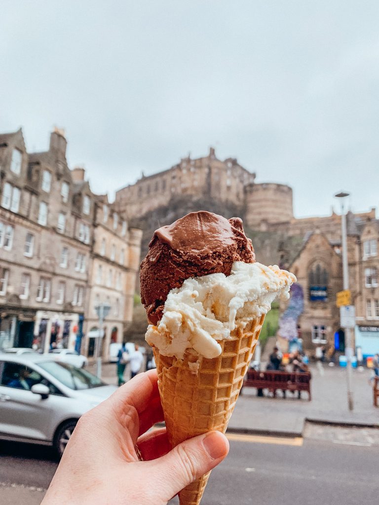 Ice cream cone being held up in the air in front of a castle on a hill
