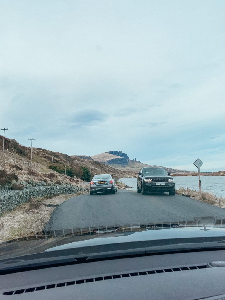 View through the windscreen of a car of a car in front and an oncoming car passing each other on a small country road next to a lake