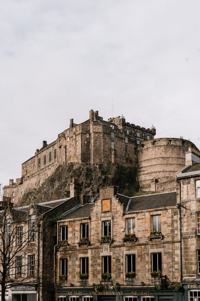 Large grey castle in hill behind row of grey, brick buildings in Edinburgh Scotland