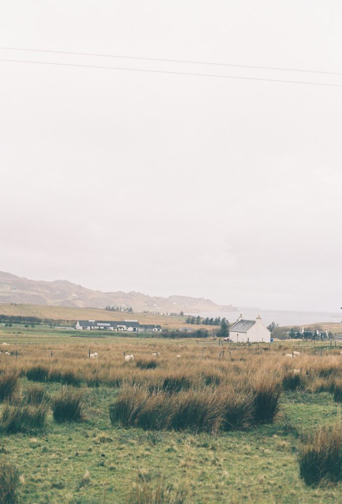Green field with an old white home with water and mountains in the background