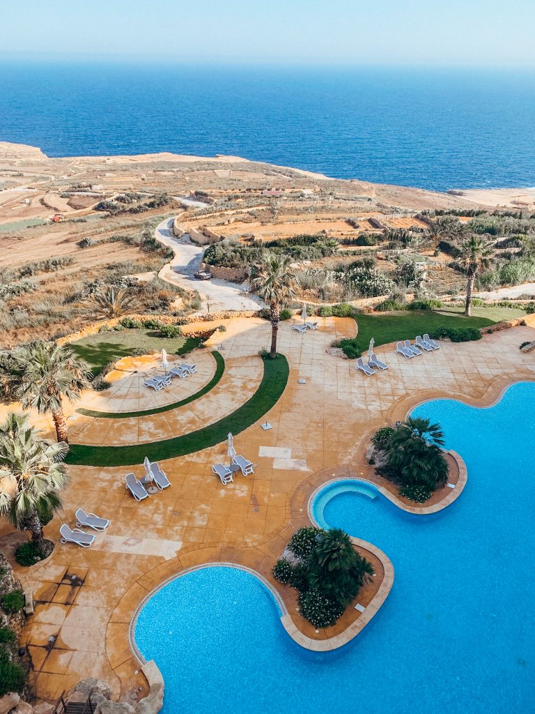 View from above of blue swimming pool next to the brown countryside next to the sea