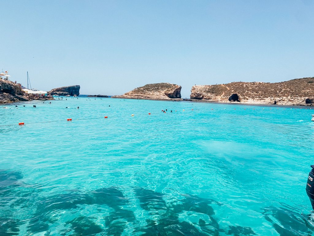 Turquoise blue water with cliffs and rock leading down to the water in the distance