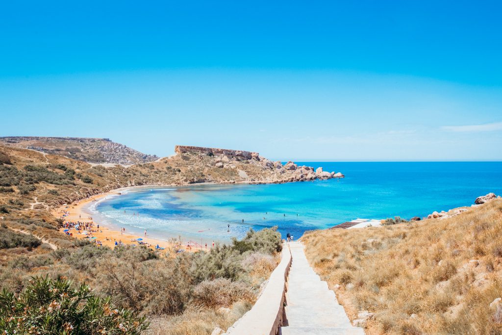 Stairs lead down to bay with blue water and golden sand in Malta