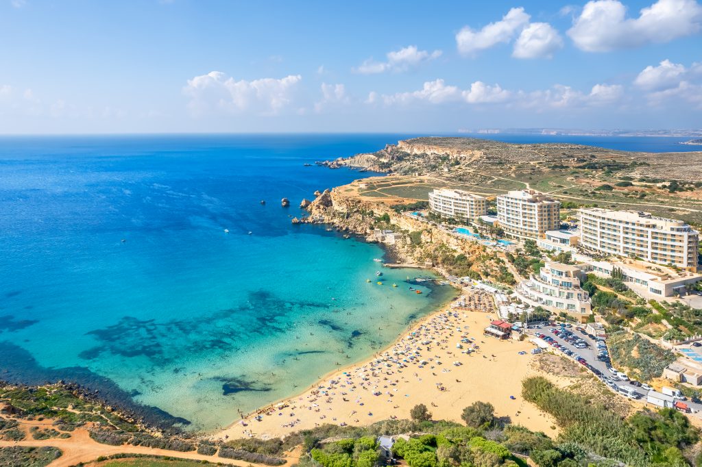 Arial view of beach with blue water and golden sand dotted with umbrellas and surrounded by hotels