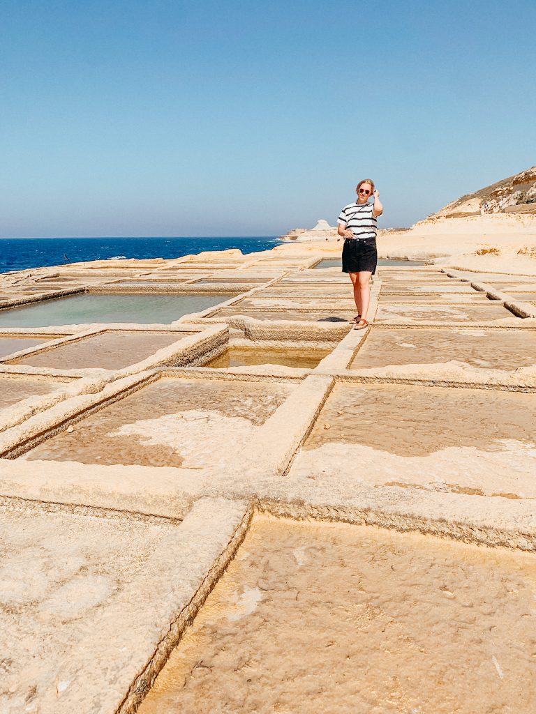 Woman walking along rocks slab with squares cut out filled with water and salt