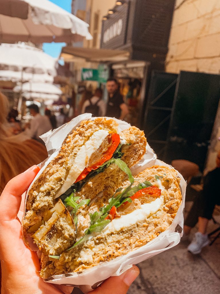 Hand holds a sandwich with a white tissue wrapping