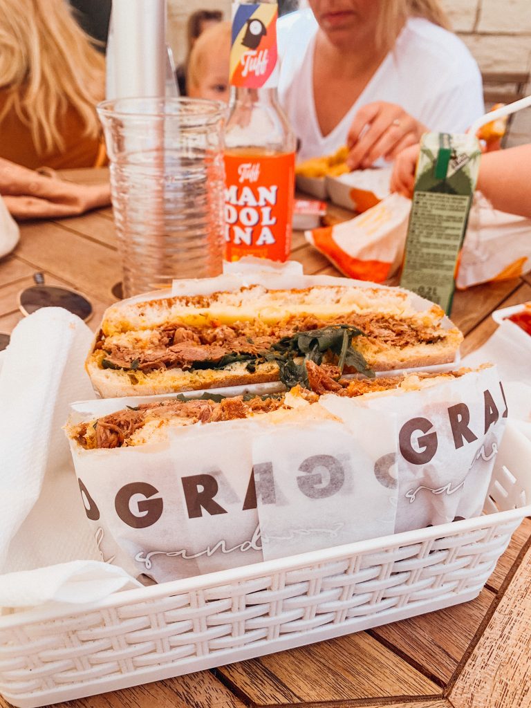 Sandwhich in a white tissue paper in a white wicker basket