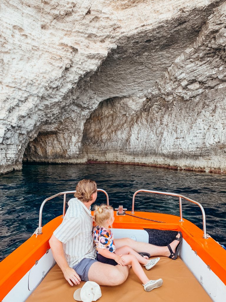 Father and child sit on orange and white boat looking out at a white cave
