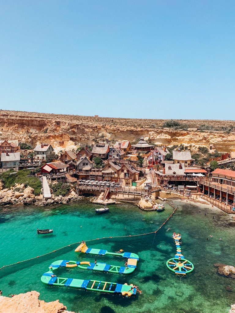 Arial view of cove lined with wooden buildings and bright green and blue water with large, colorful obstacle course