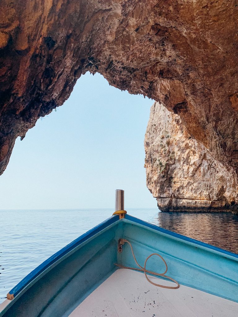Bow of blue and white boat goes under large rock arch