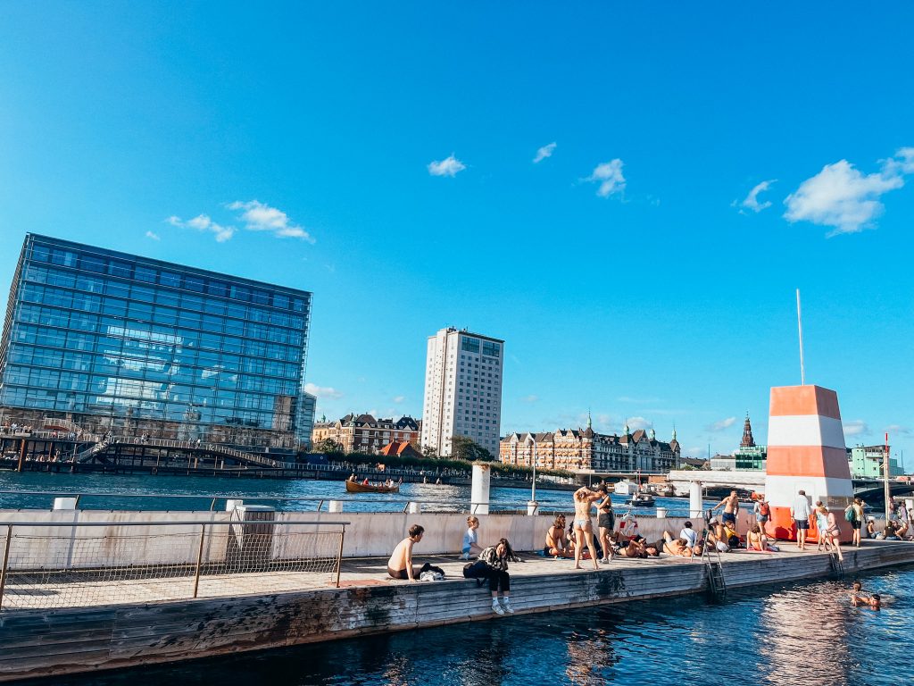 People sit along the side of an outdoor pool next to the harbor in Copenhagen