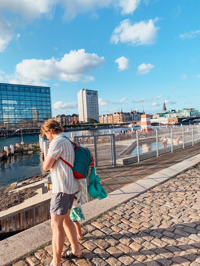 Man walks along pathway next to a harbor on a sunny day