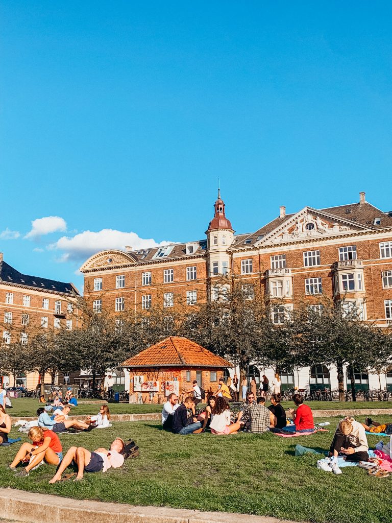 Small red brick building in a grassy lawn covered in people picnicing