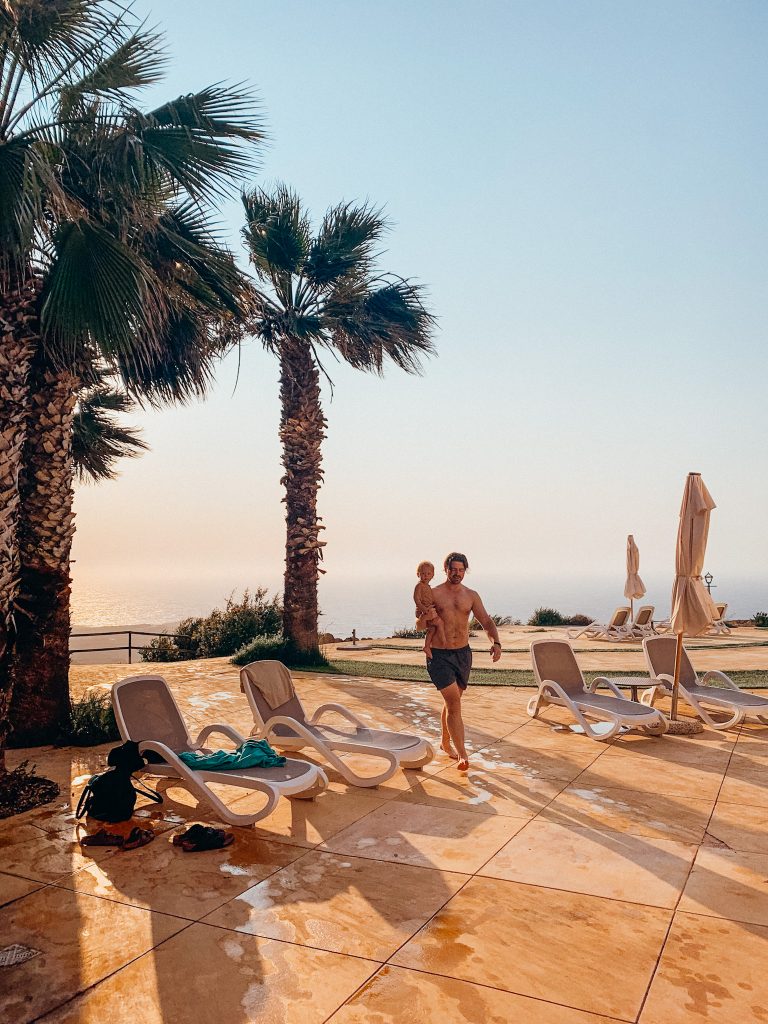 Man walks with child next to palm trees and pool lounge chairs