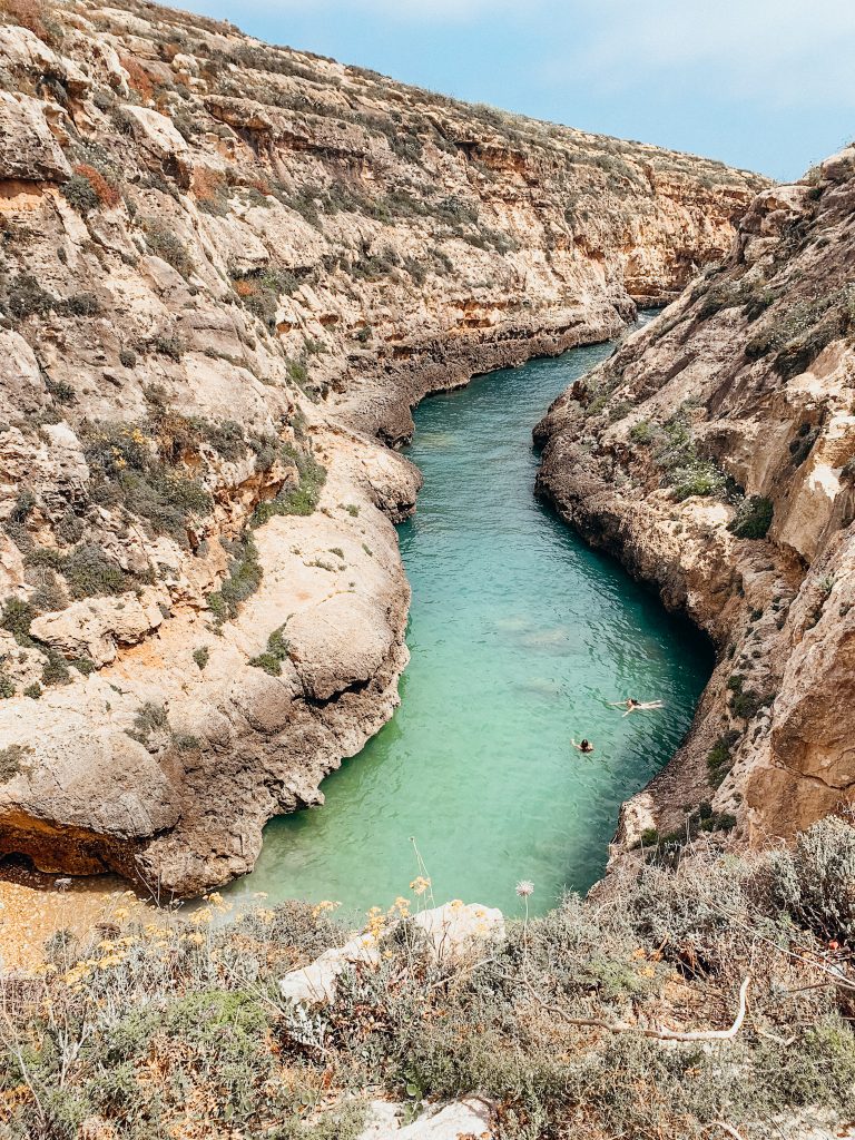 Tan canyon with people swimming in green sea water at the bottom