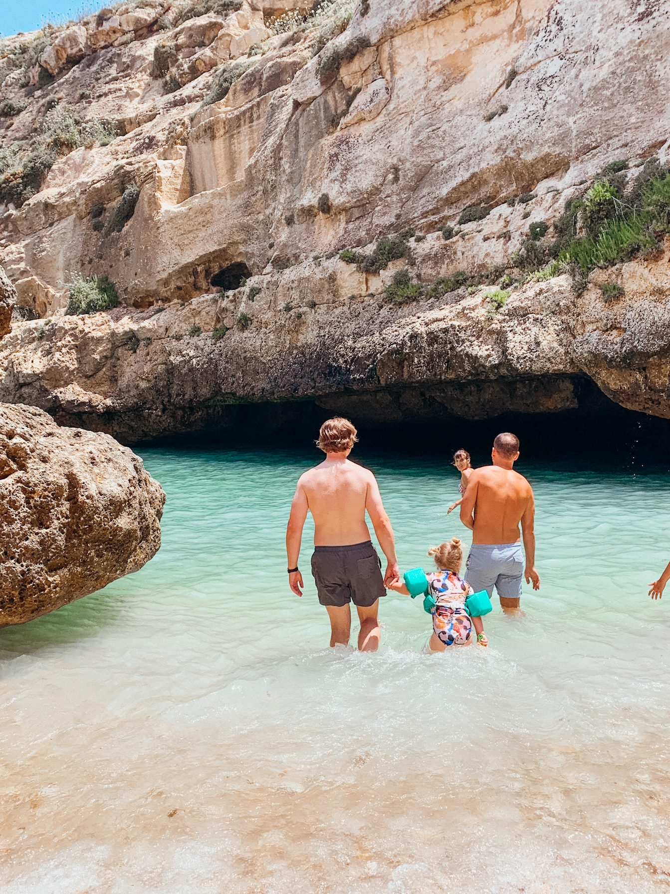 Man walks with child into green water lined with cliffs