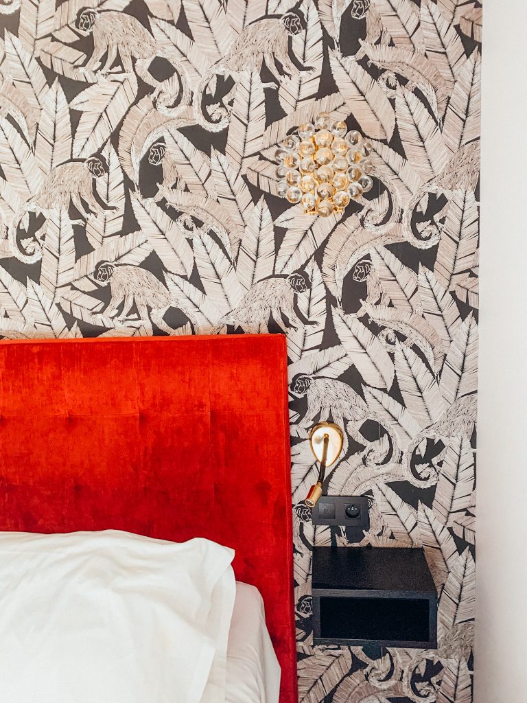 Red headboard next to bed with white sheets in front of black and white wallpapered wall at Rayz Eiffel Hotel