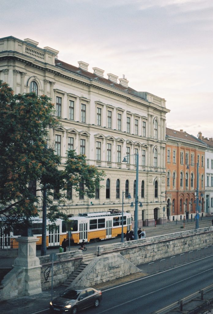 Yellow and white tram in front of old white brick building in Budapest