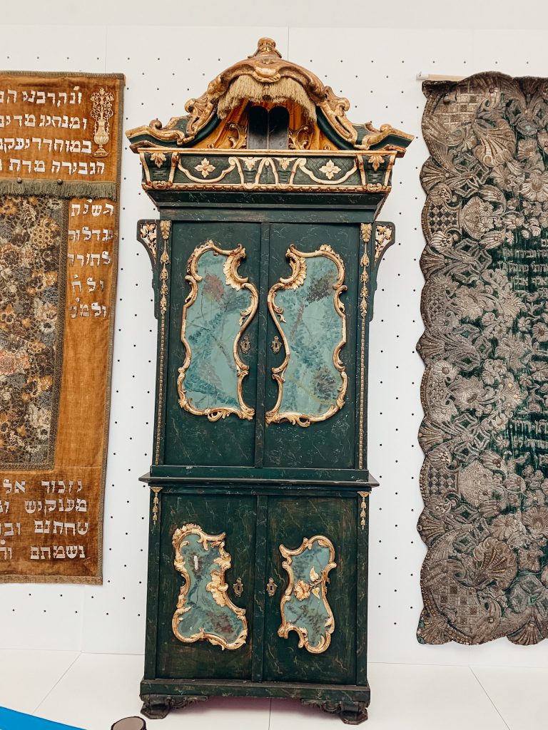 Large green cabinet with ornate gold trim in front of a white wall
