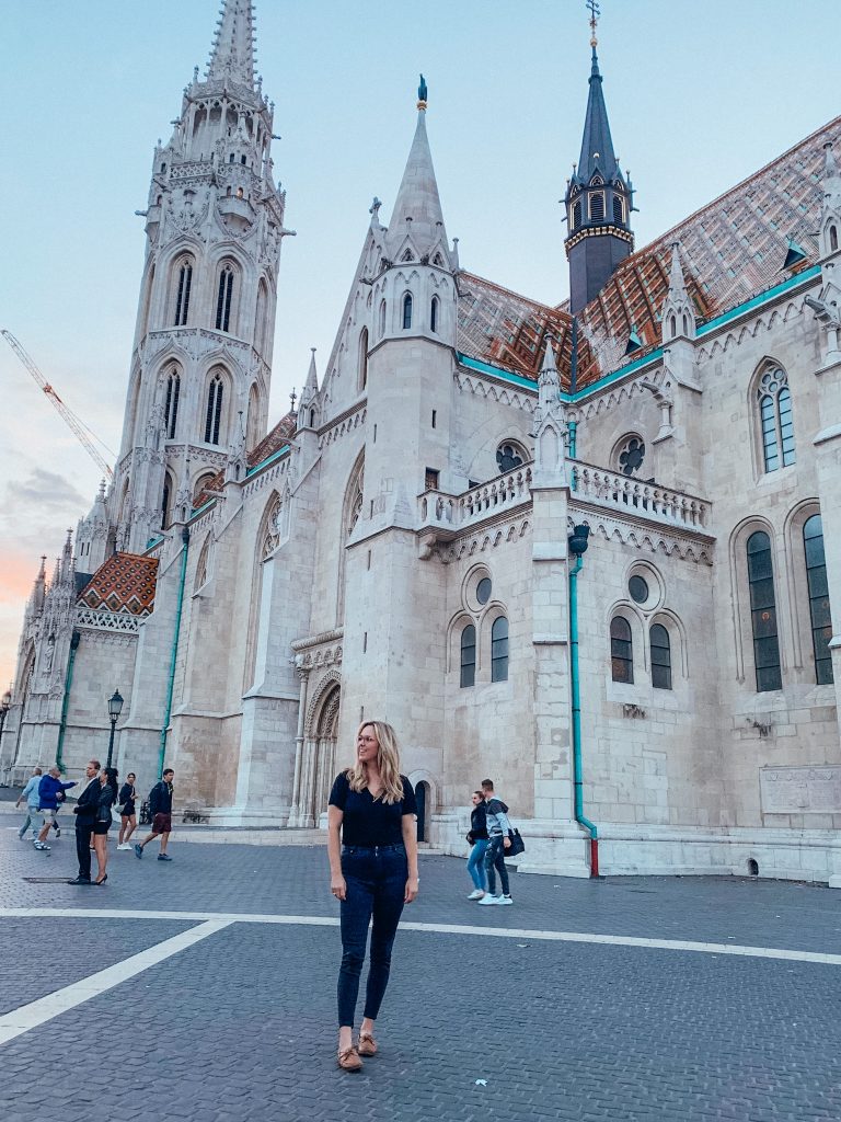 Woman in black standing in front white church with spires and brown and turquoise roof shingles