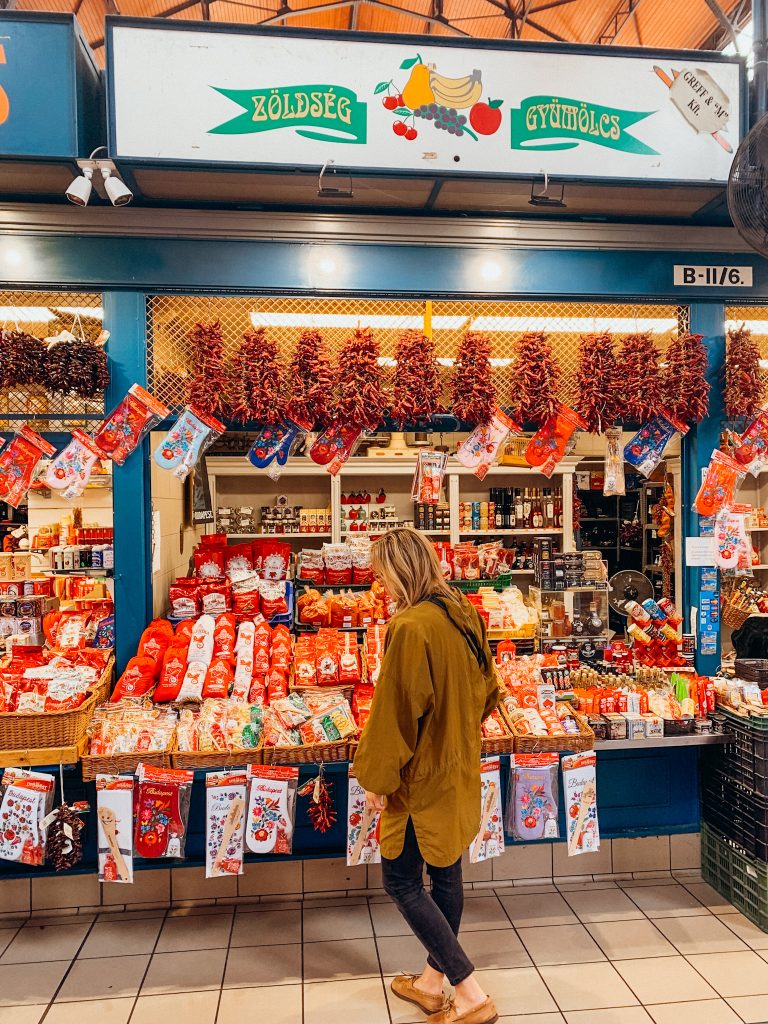 Woman in yellow packets stands in front of market booth selling packets of paprika spices
