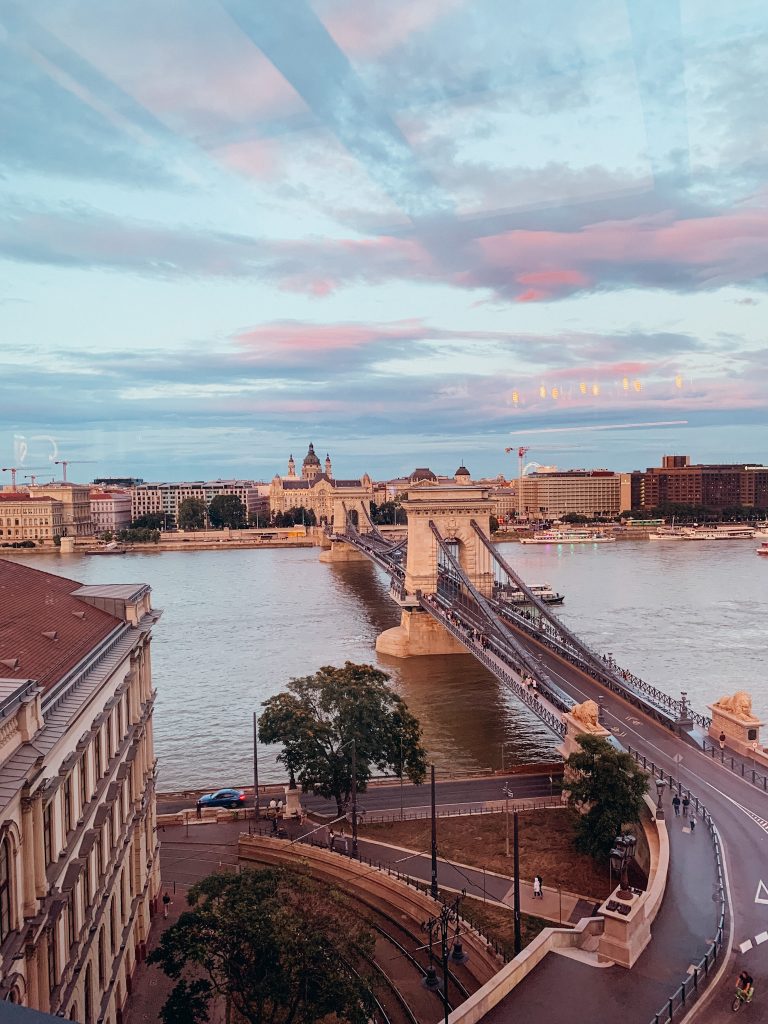 A vehicle bridge with two white arches over a large river at dusk