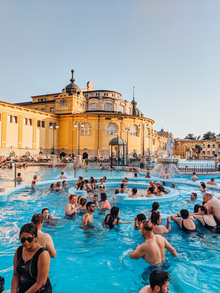 People standing in blue pool with large yellow building in the background