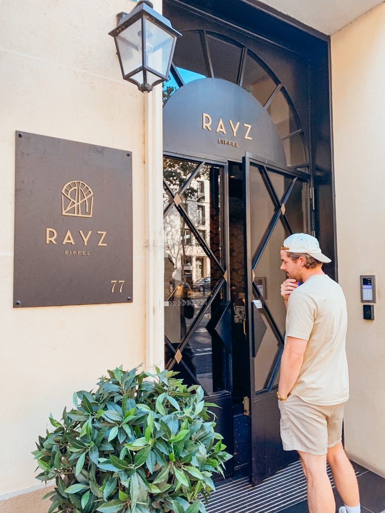 Man stands in front of black hotel doors near sign that reads 'Rays Eiffel'